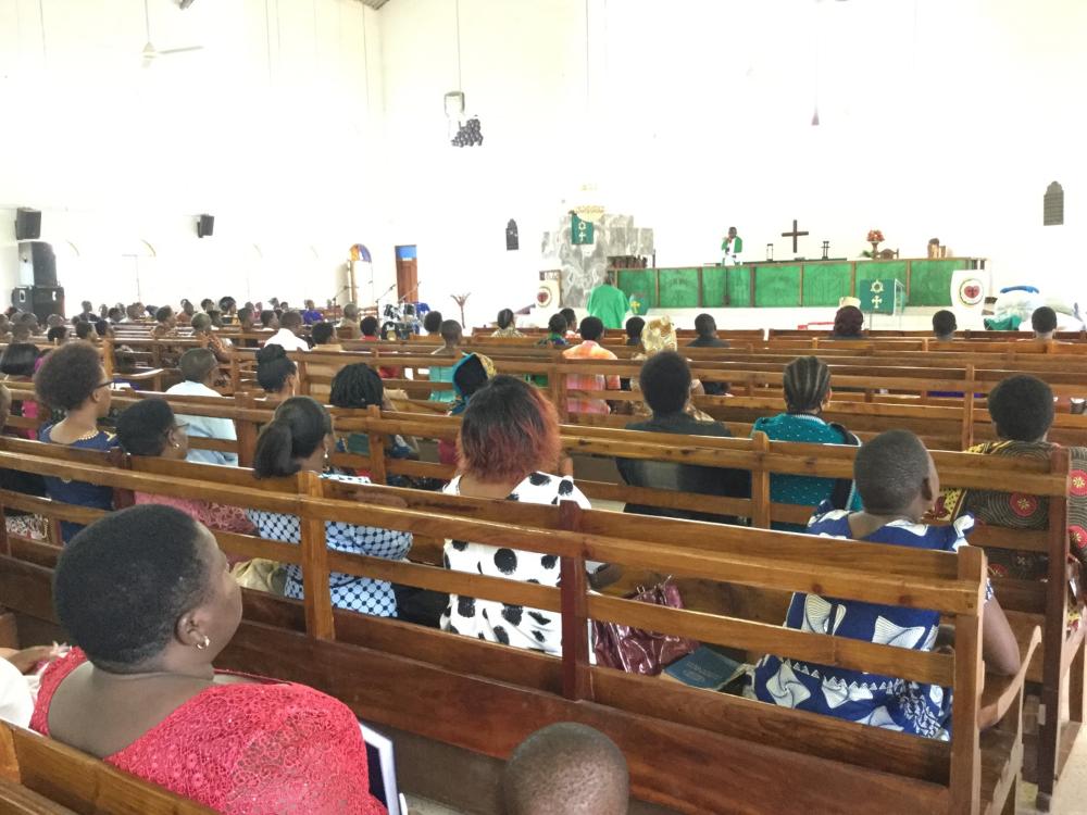 Människor deltar i gudstjänsten i Tanzania. De sitter på kyrkobänkar i ett stort utrymme.