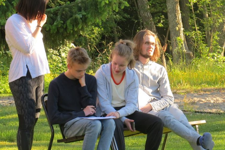 Tre ungdomar sitter på en bänk utomhus och en flicka står bredvid.