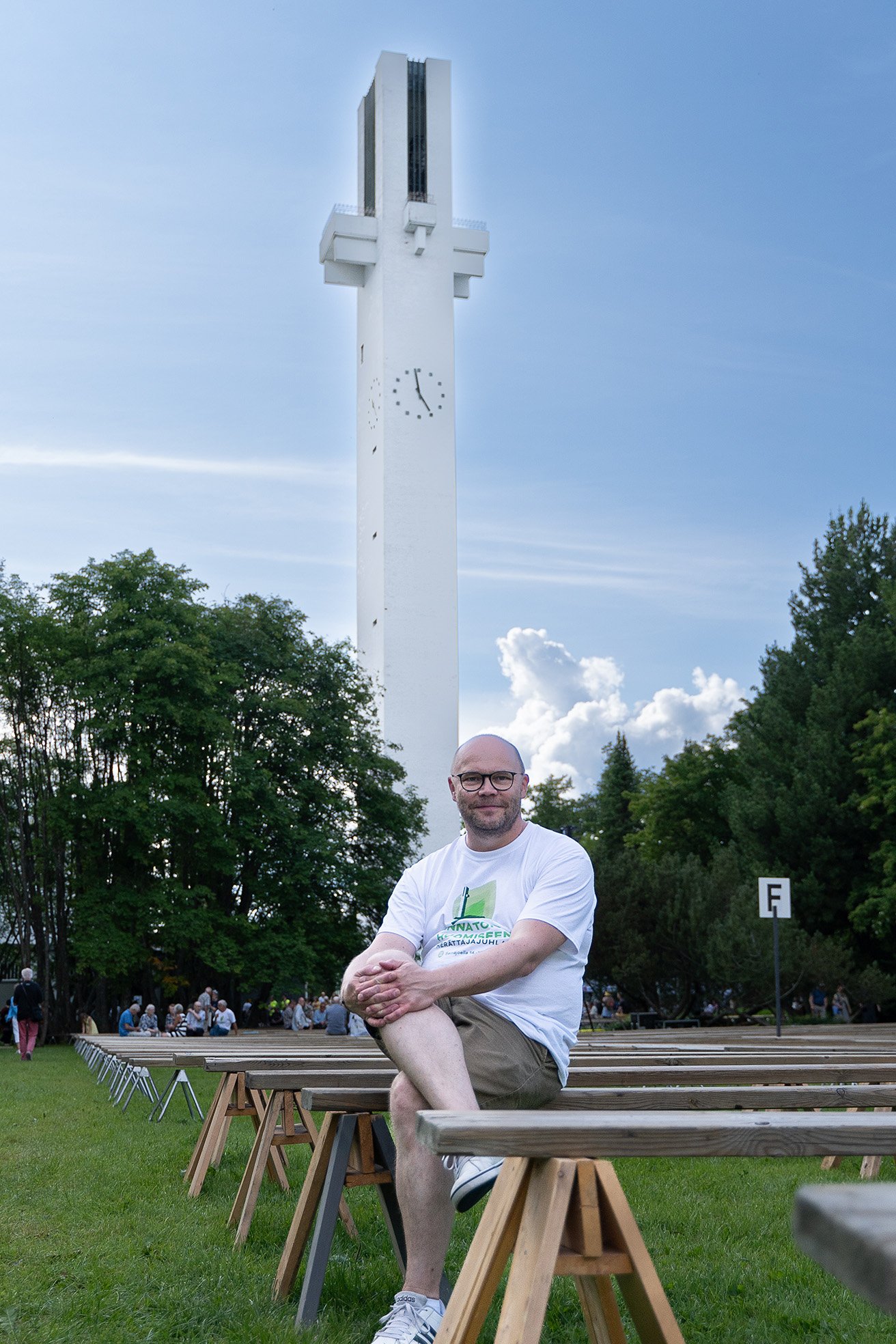 Jani Kela sitter på en bänk. I bakgrunden ett stort vitt kors.