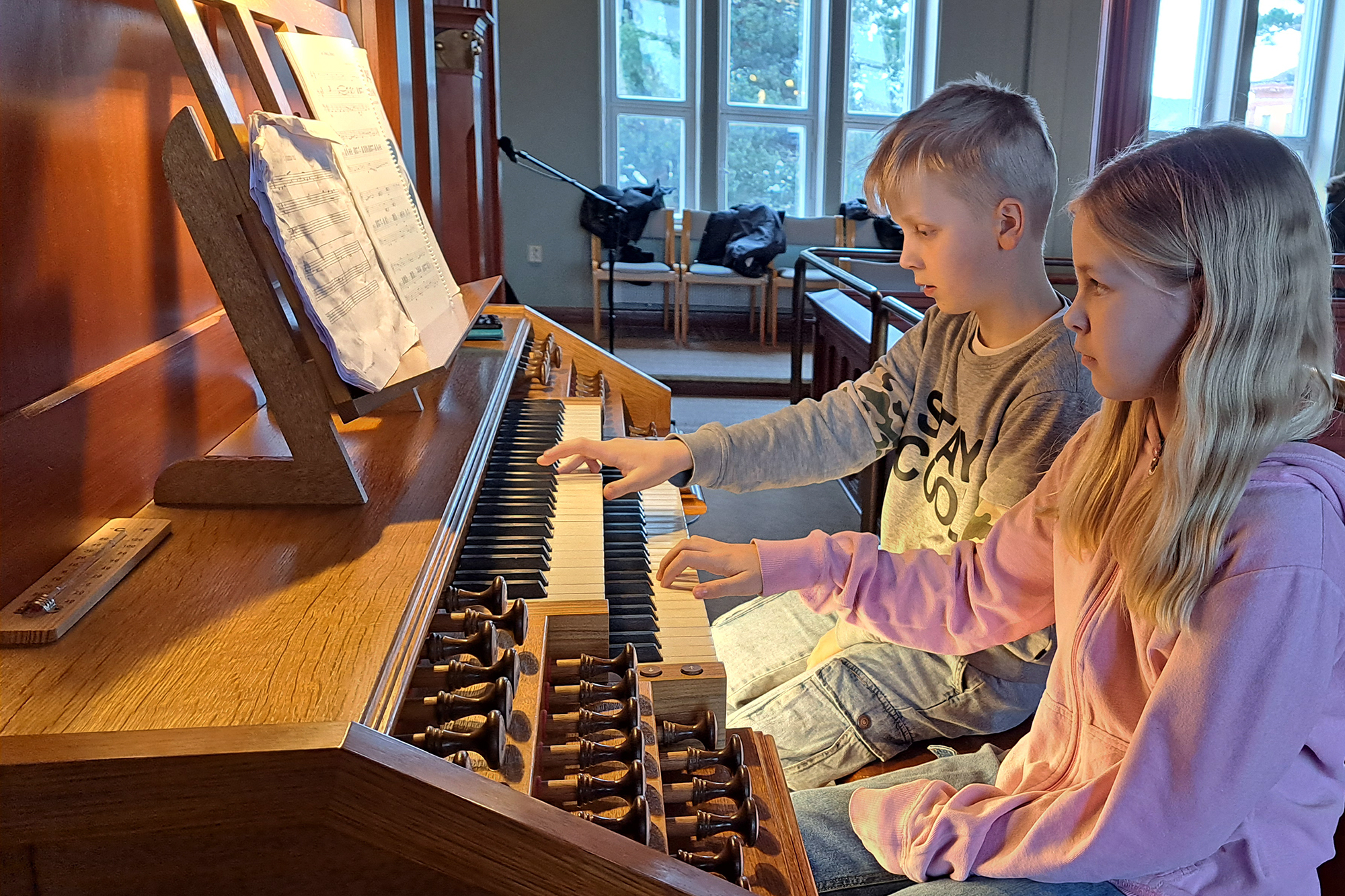 En flicka och en pojke spelar på en kyrkorgel.