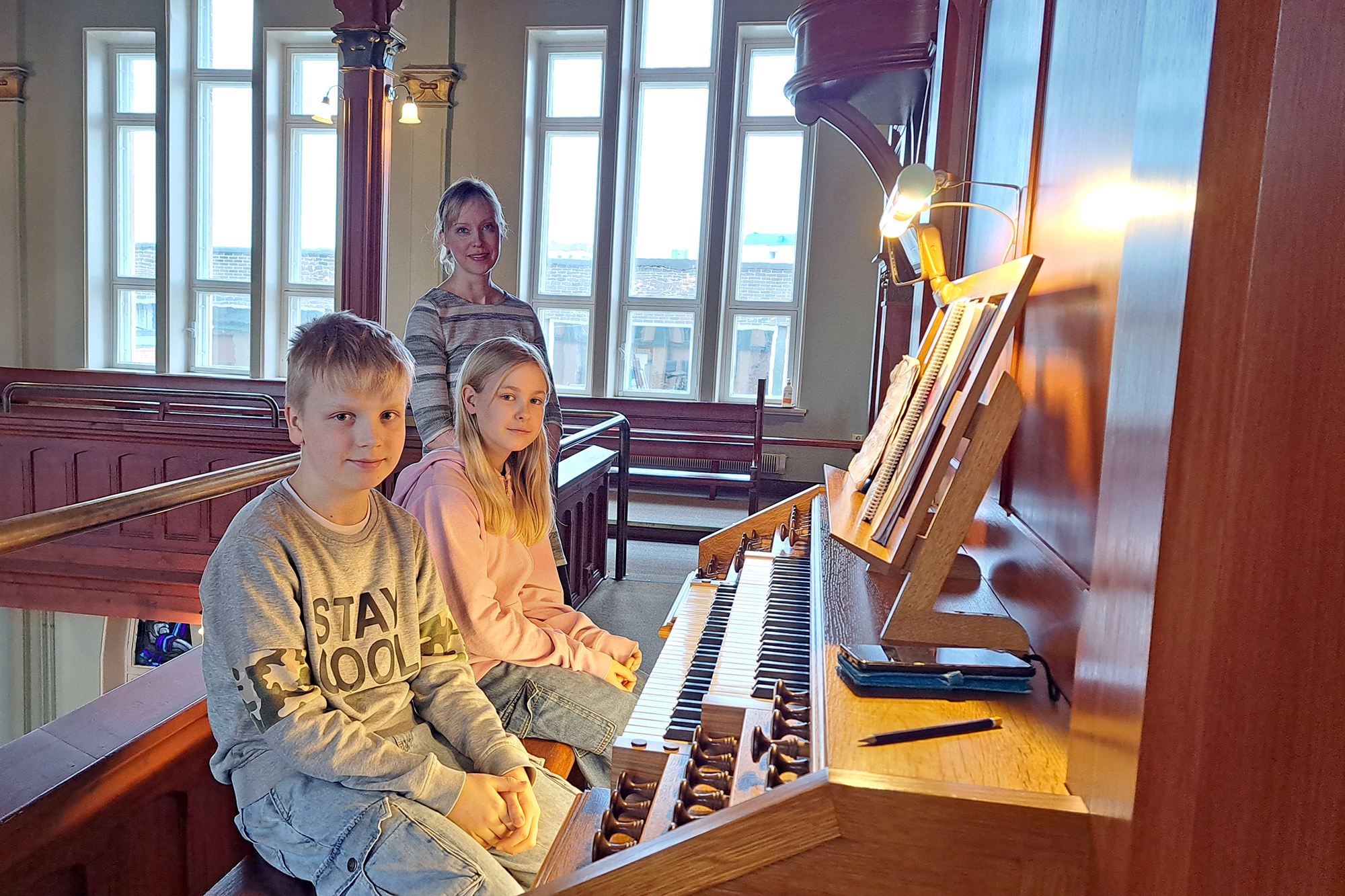 Två barn spelar på en kyrkorgel. I bakgrunden en kvinna.