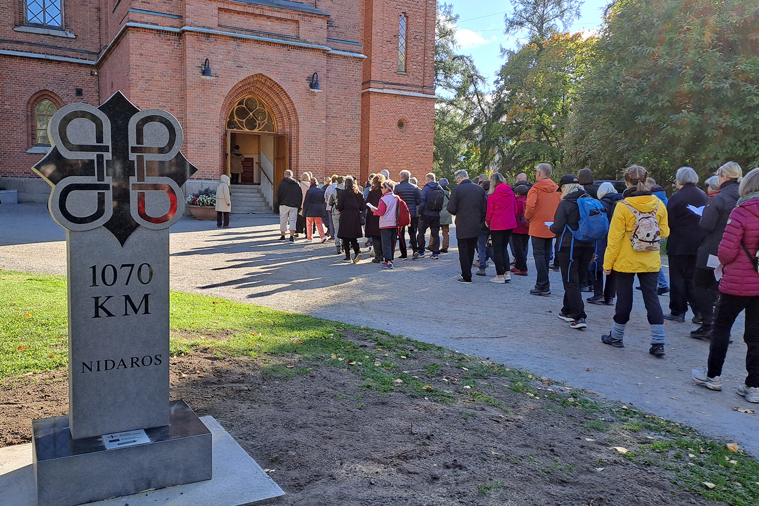 Männi går in i en kyrka. I förgrunden en sten med texten: 1070 kim Nidaros.