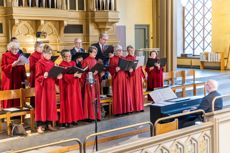 Kör iklädd röda kördräkter sjunger i en kyrka.