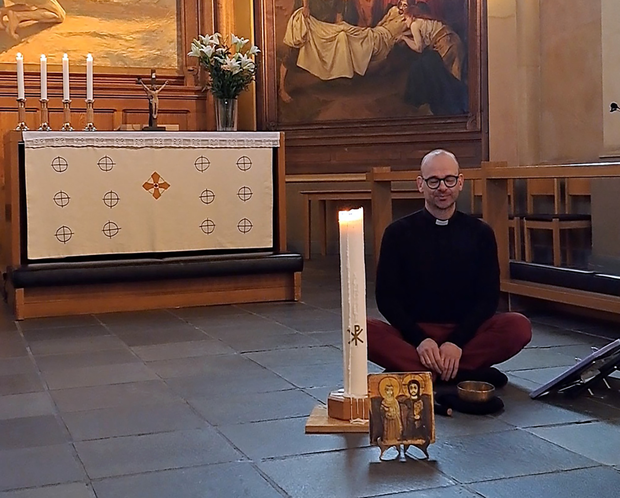 Man sitter med benen i kors i en kyrka. Framför honom finns en ikon, ett ljus och en klangskål.