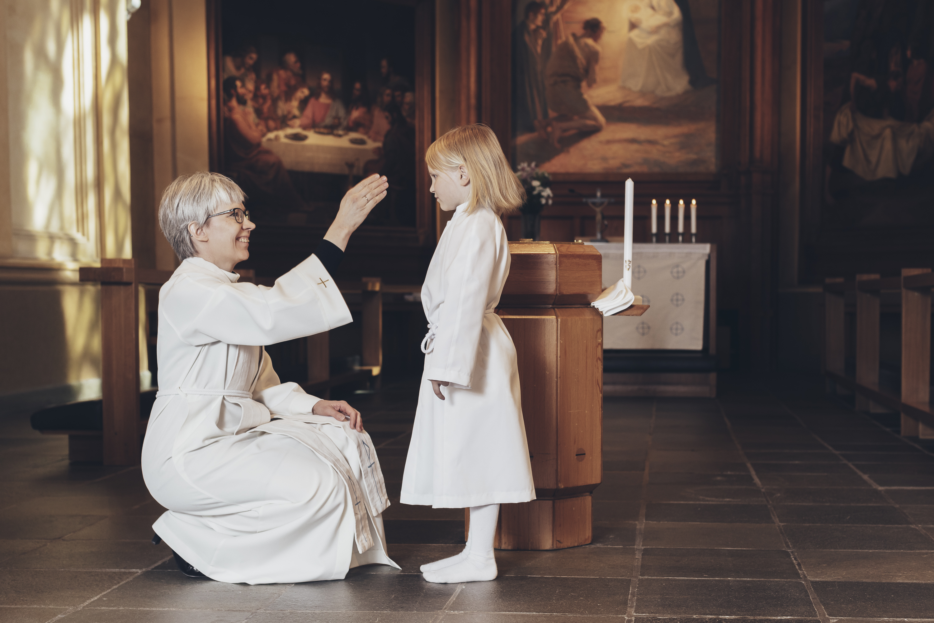 Morgondop En präst välsignar en liten flicka framme i en kyrka. Flickan står på golvet framför prästen.