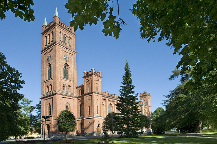 Röd tegelkyrka i nygotisk stil med högt torn med fyra kyrkspiror vid huvudingången. Ljusgrönt plåttak.