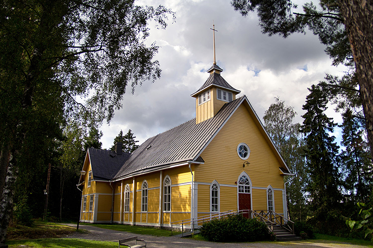 Gul träkyrka med mörkbrunt plåttak.