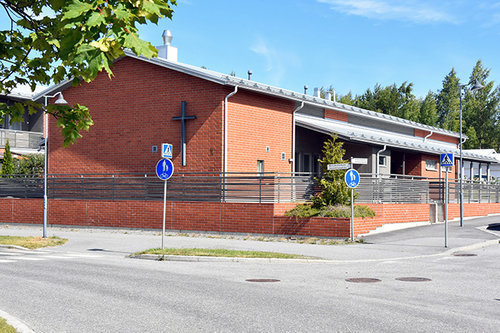 Skogsbergets församlingshem Låg röd tegelbyggnad med kors på väggen
