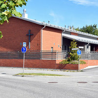 Skogsbergets församlingshem Låg röd tegelbyggnad med kors på väggen