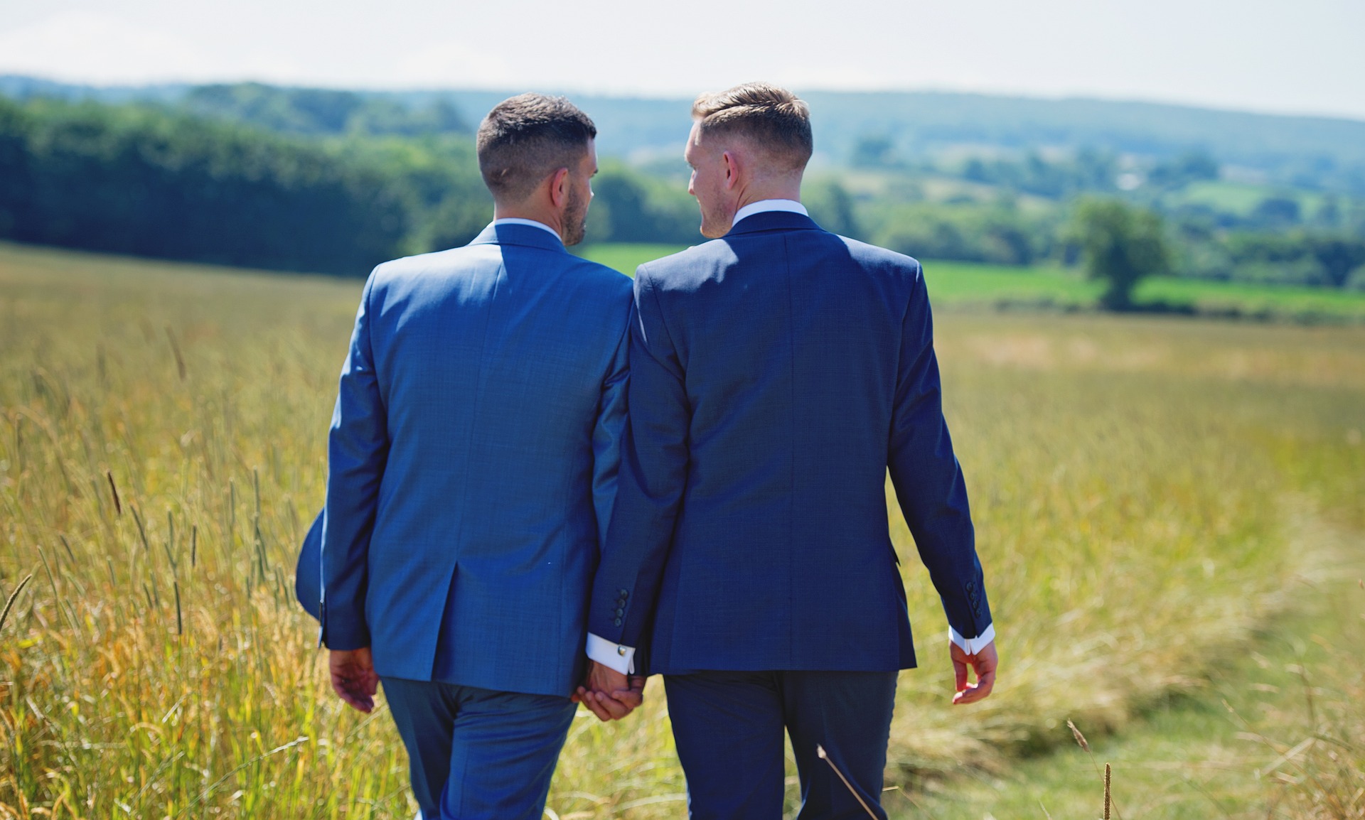 Två män klädda i kostym håller händerna och går på en äng.