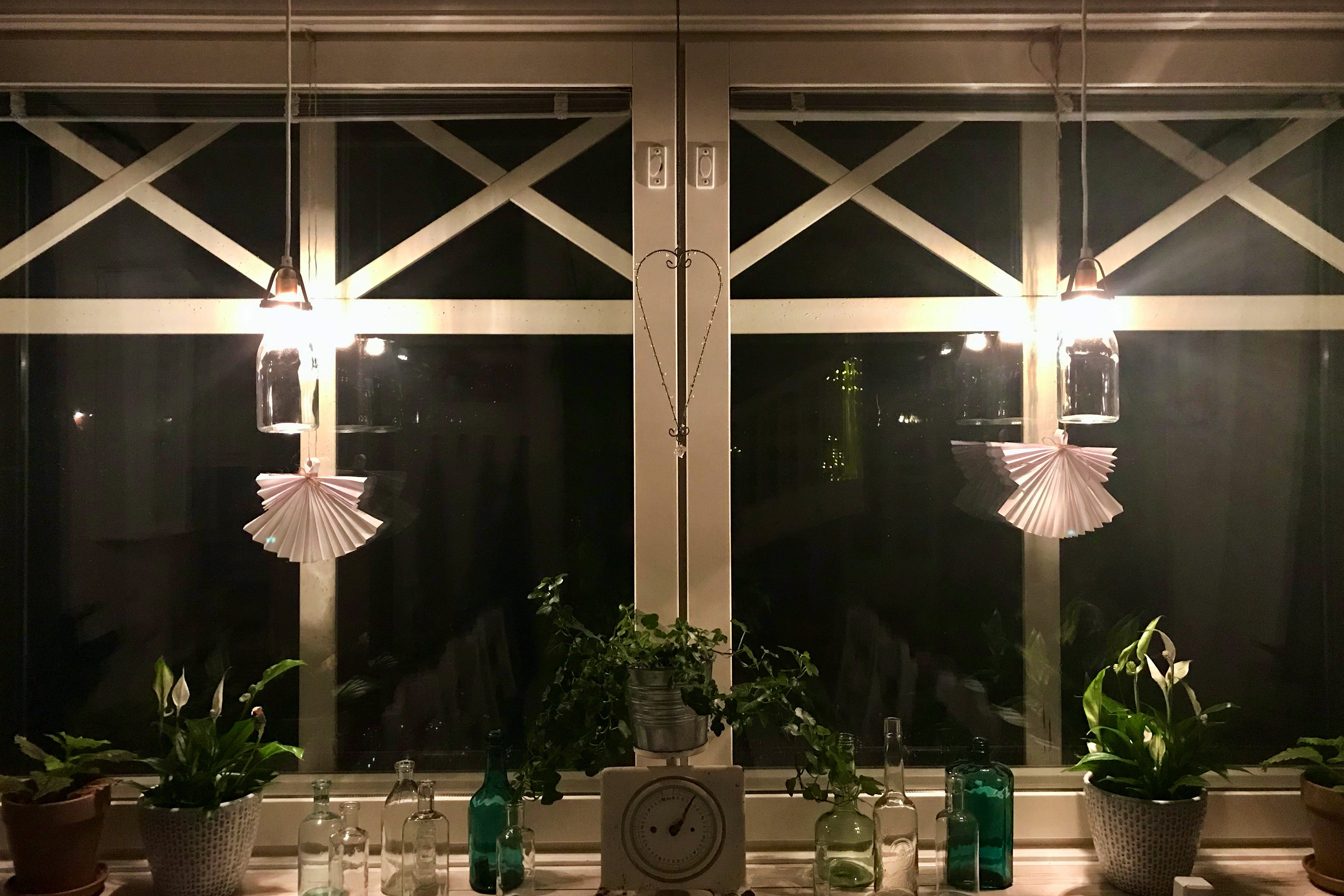 Två vikta vita pappersänglar som hänger i ett dubbelfönster.