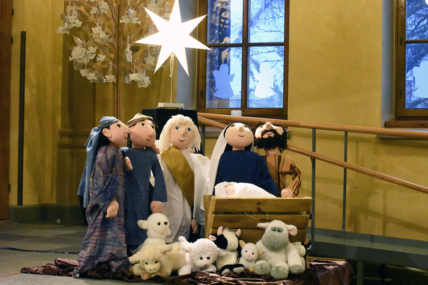 En julkrubba med tygdockor föreställande Jesusbarnet, Maria, Josef, ängel, herdar och får.
