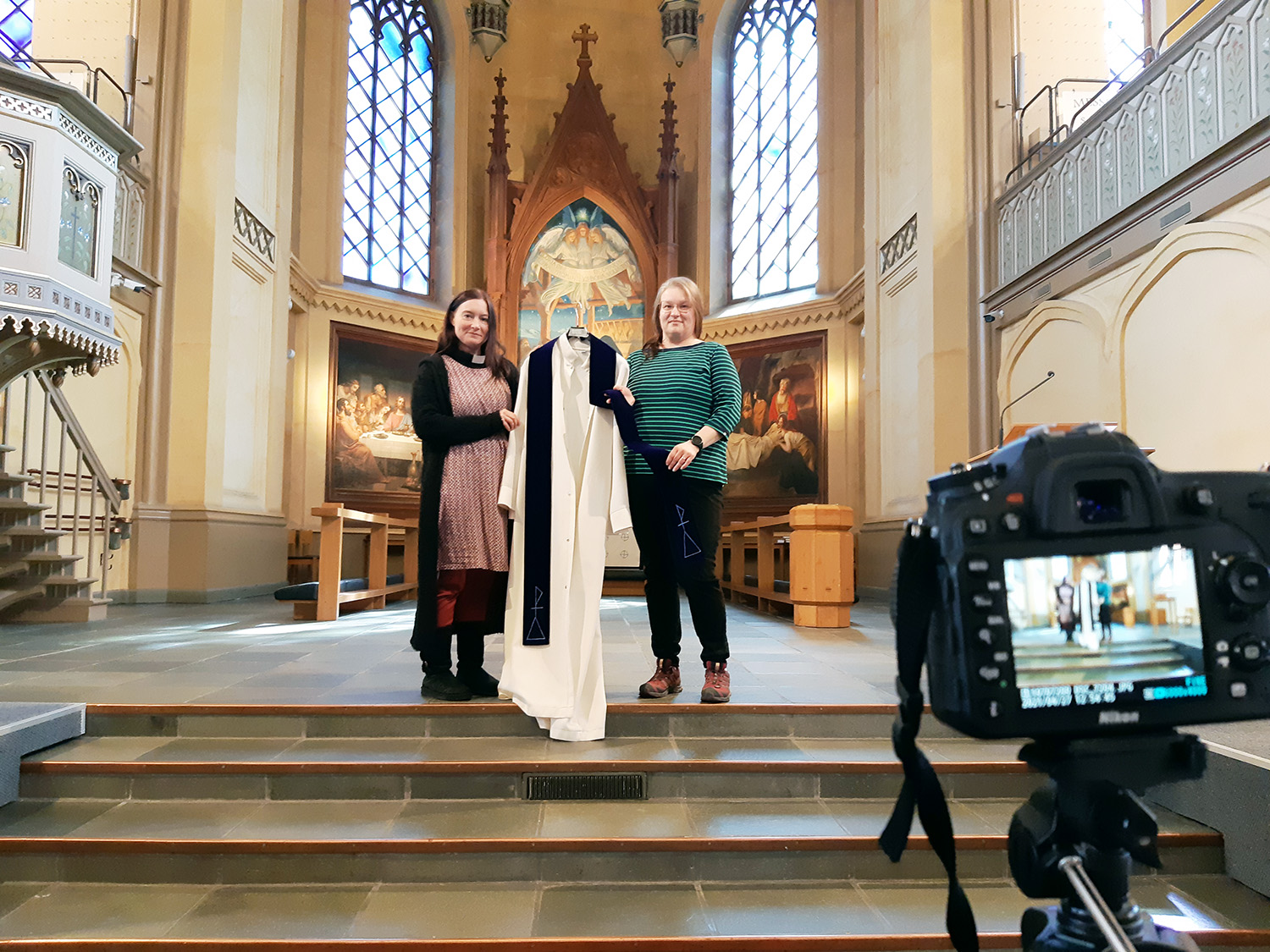 Två kvinnor håller i en alba i en kyrka.