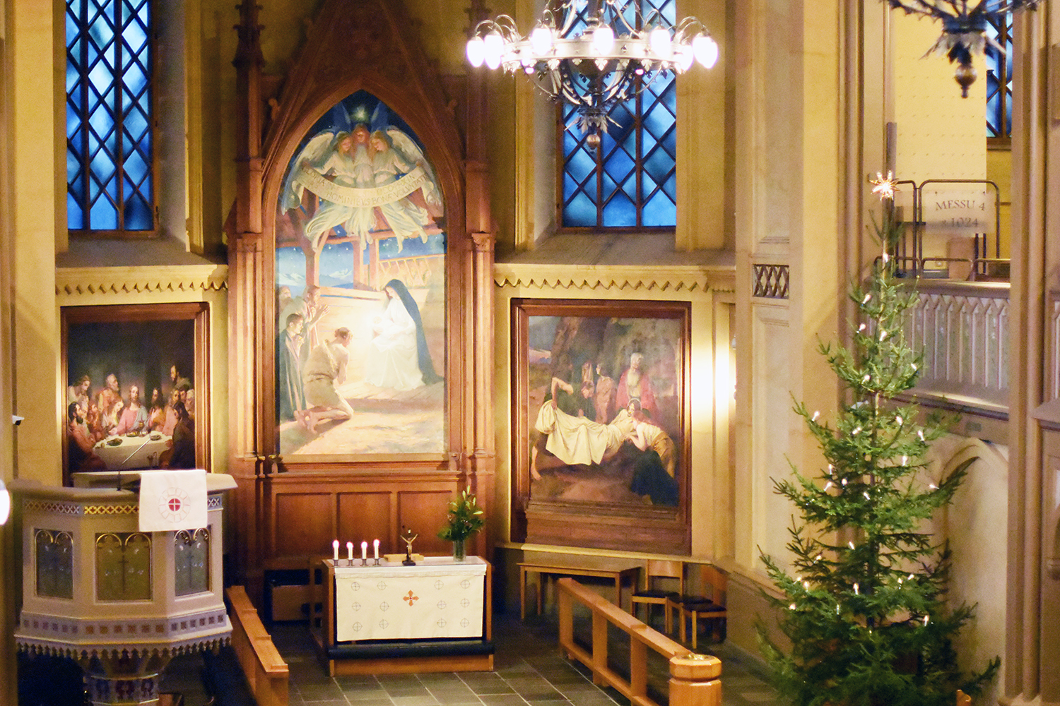Julgran med lampor i Trefaldighetskyrkan famför altaret och altartavlorna. Altaret har vit altarduk.
