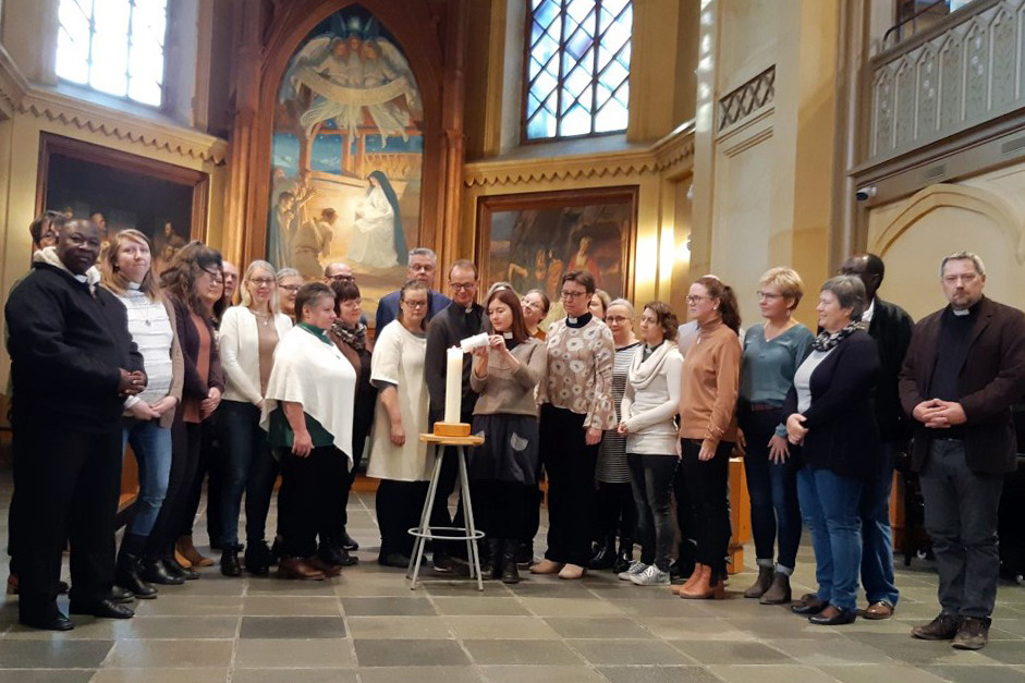 En skara människor står samlade i en kyrka. I bakgrunden syns altartavlan.