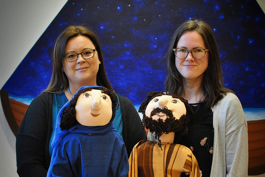 Två leende kvinnor håller i två dockor som föreställer Maria och Josef.