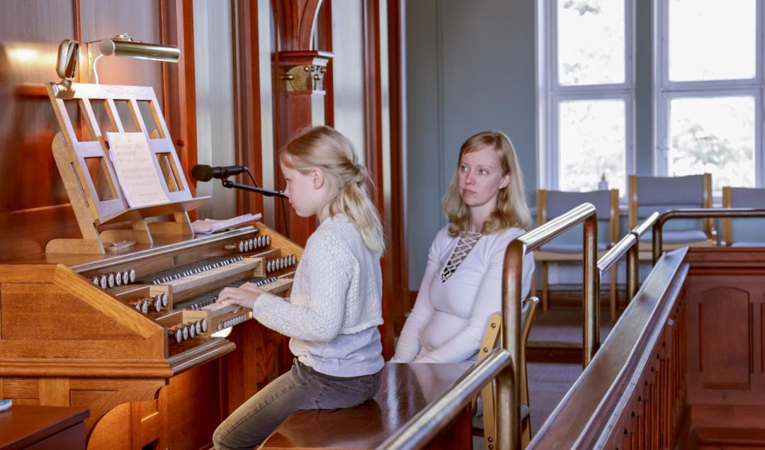 Flicka spela orgel. En kvinna sitter bredvid henne.