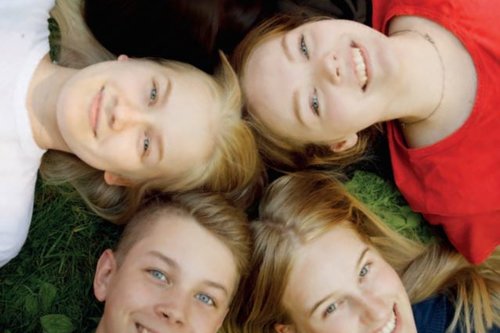 Fyra ungdomar ligger i en ring med huvudena i mitten. Endast de glada ansiktena syns. Länk till webbsida om konfirmandarbete i kyrkan.
