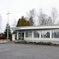 Siltaranta Låg, vit träbyggnad med stora fönster. På gårdsplanen finns ett stort vitt kors.