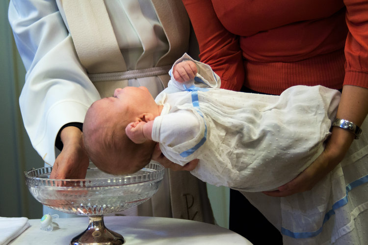 Baby hålls ovanför dopfunt, präst sätter vatten på huvudet. Länken leder till webbsidan om dop.