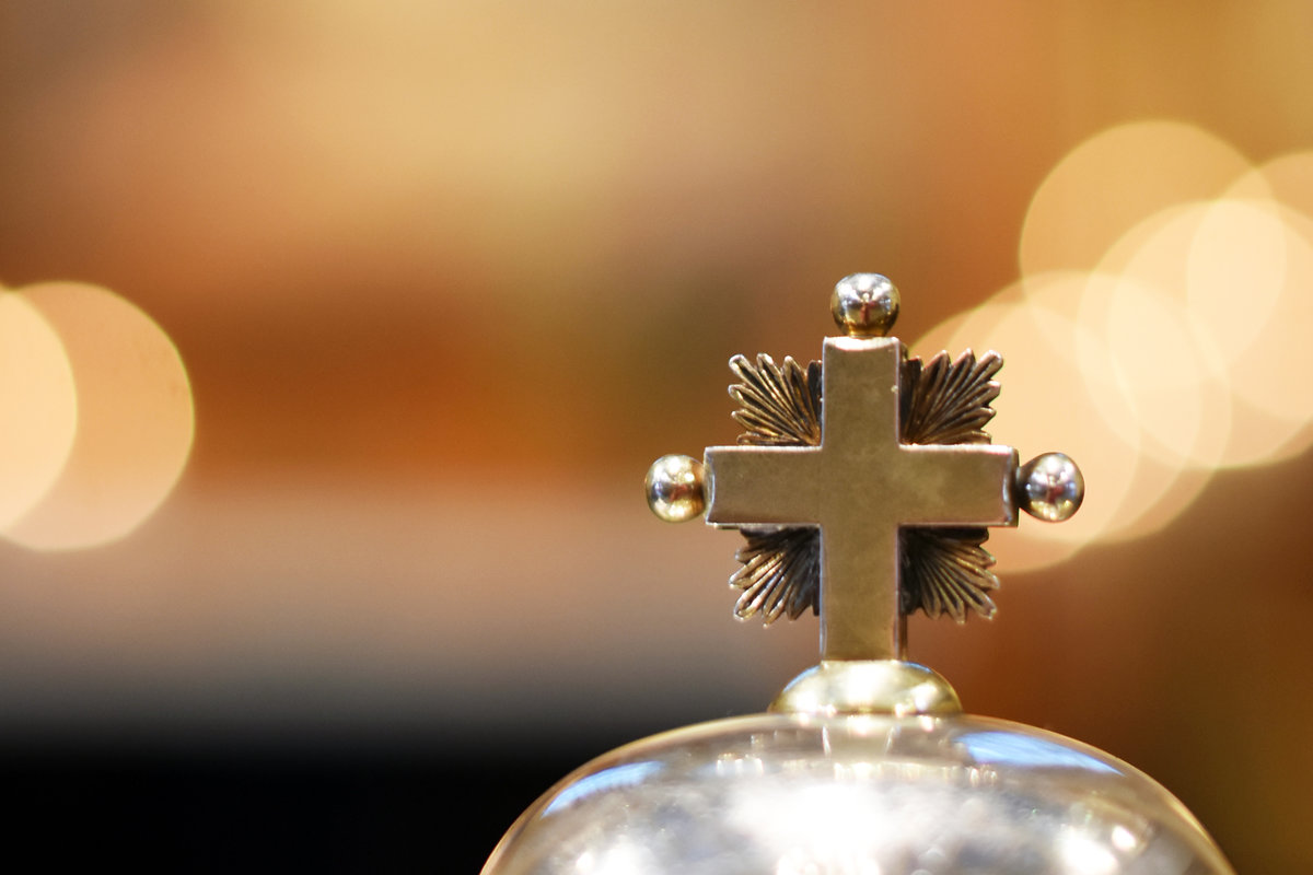 Närbild av silverkors som finns på locket till en skål som innehåller oblater.