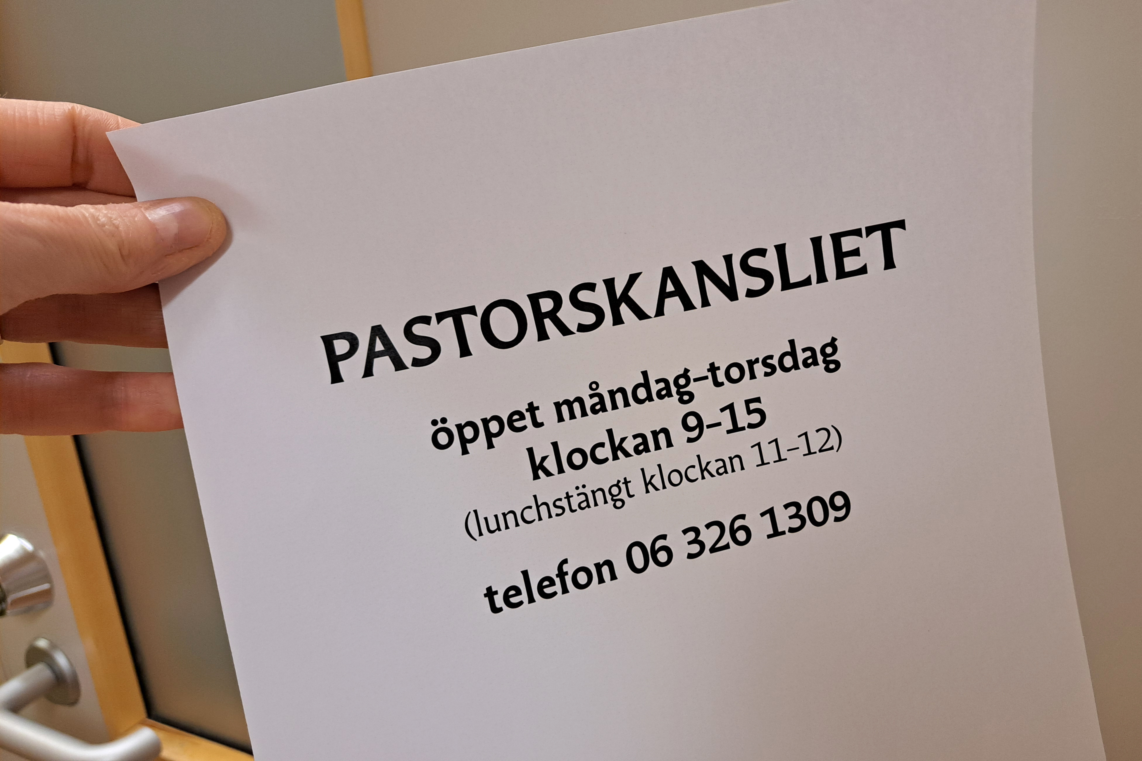 Hand håller i lapp med text om pastorskansliets öppettider.