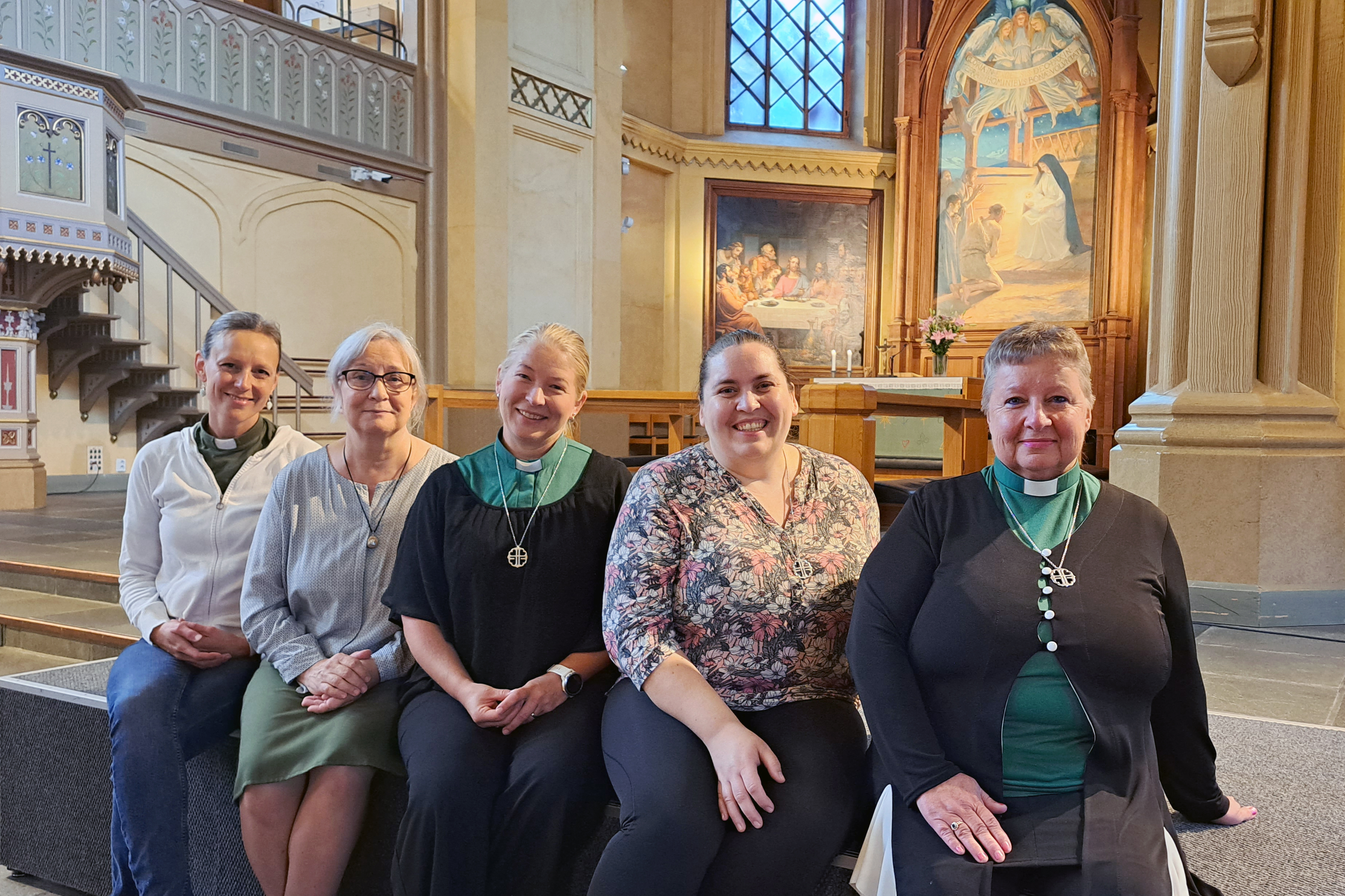 Fem kvinnor sitter på en bänk framför ett altare i en kyrka.