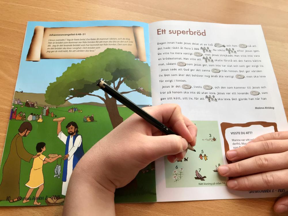 Hand som håller i en penna och gör uppgifter i en bok. Rubrik på uppslaget: ett superbröd.