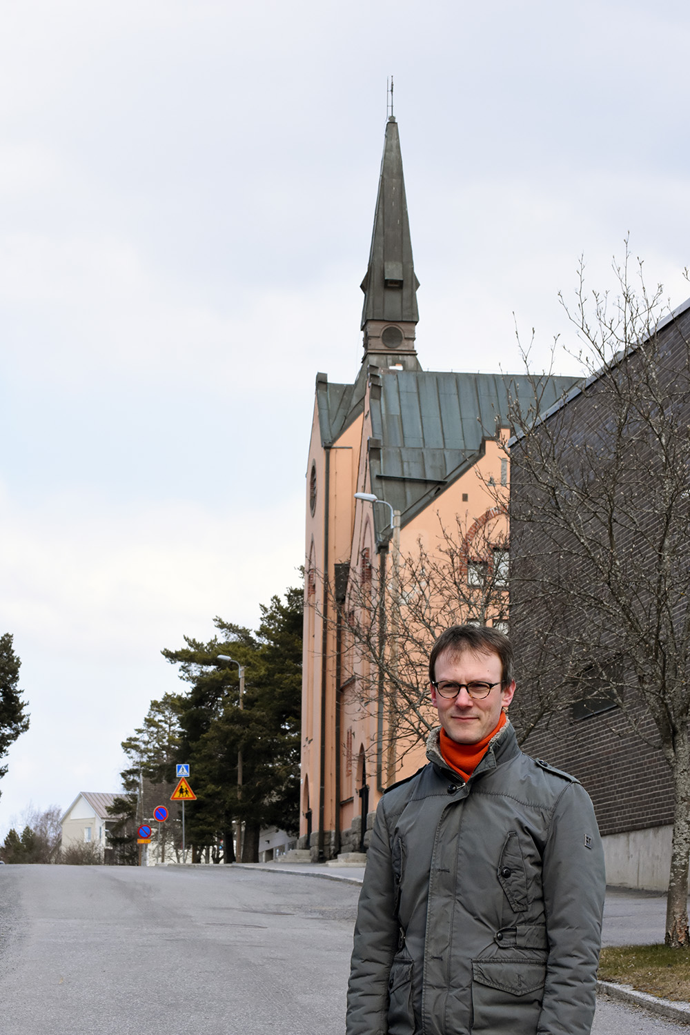 Kim-Erik Berts står på vägen framför Brändö kyrka. Det är tidg vår och träden har ännu inte fått löv.