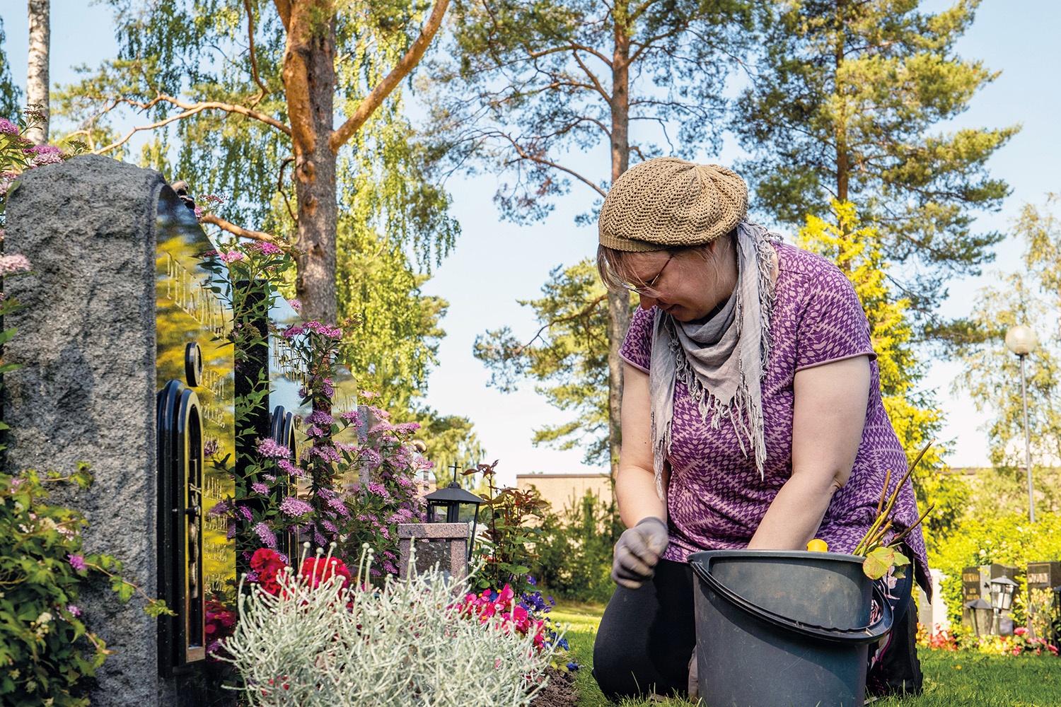 Hannele Back rensar ogräs på en grav i en lummig del av gravgården.