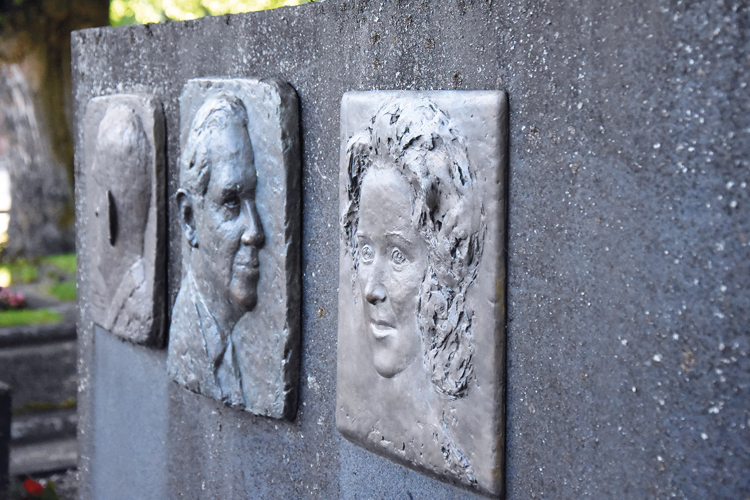 Reliefer på en grå gravsten av Eero, Tauno och Irma Rewell.