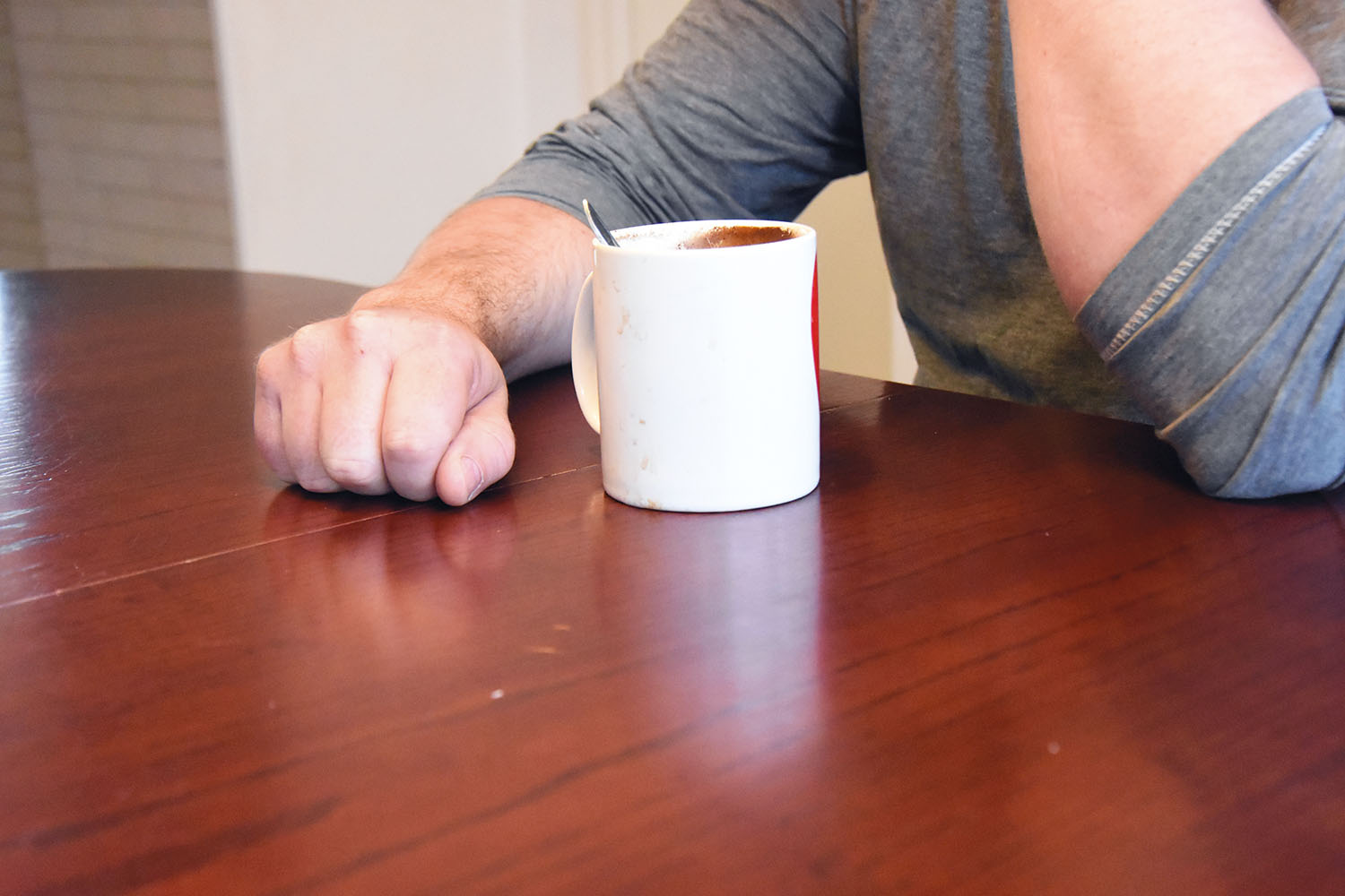 En man vid ett bord hållande i en kaffekopp. Ansiktet syns inte.