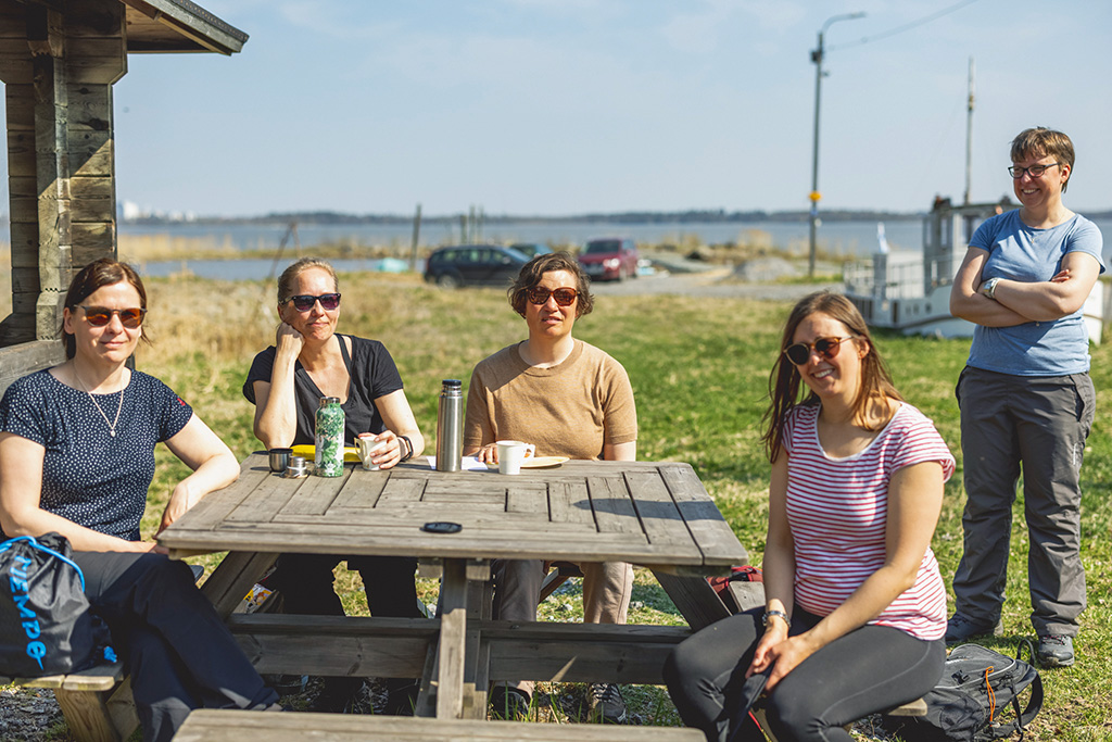 Fyra kvinnor sitter kring ett bord, en står bredvid.