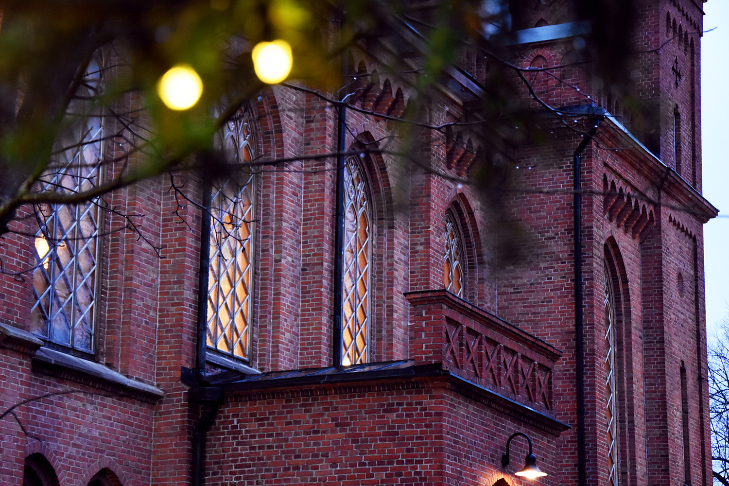 Närbild av kyrkofönster i en röd tegelkyrka.Ljuset inne i kyrkan är tänt.