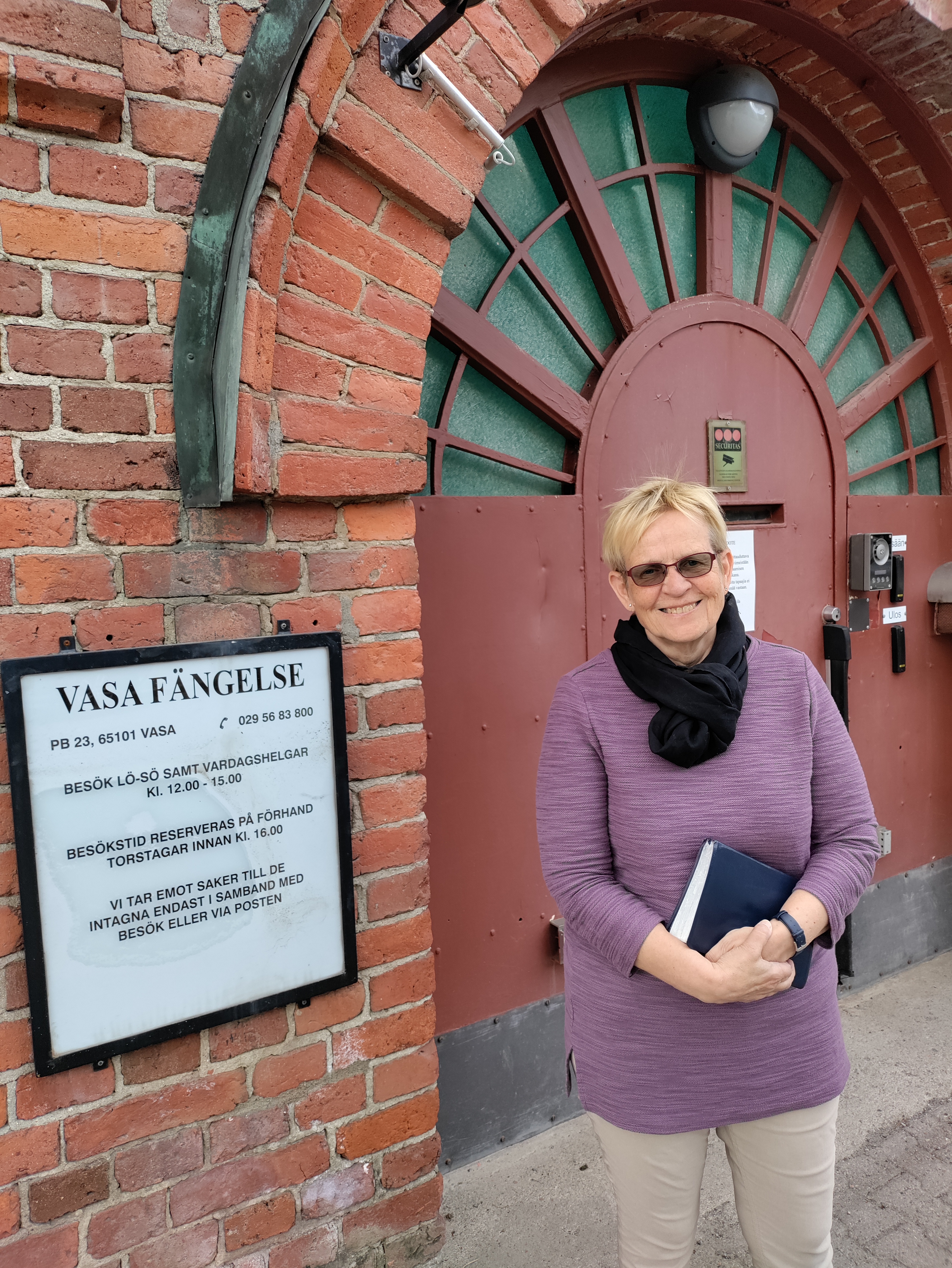 Kvinna med bok i handen stående utanför ett fängelse.