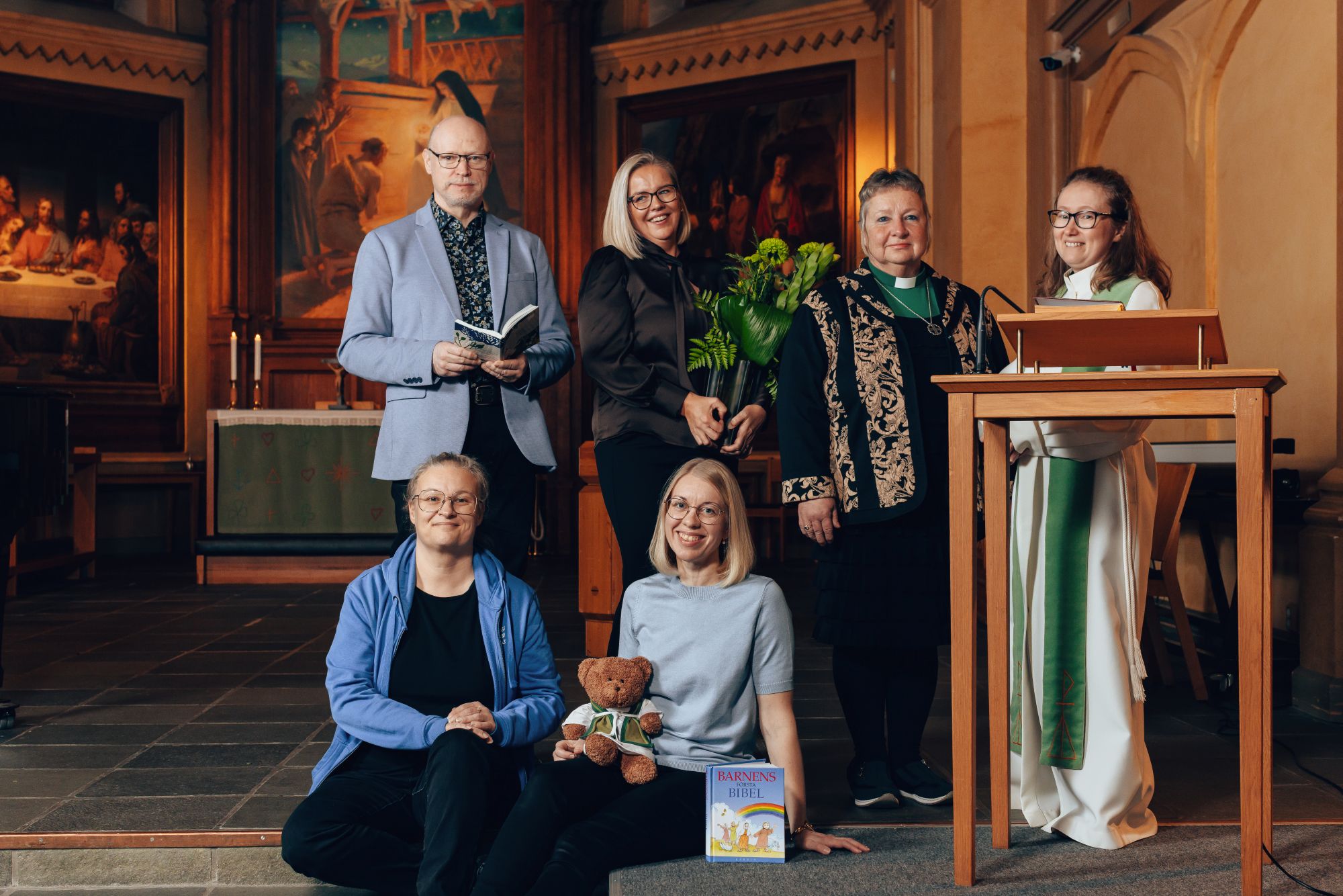 Grupp med människor står och sitter i en kyrka.
