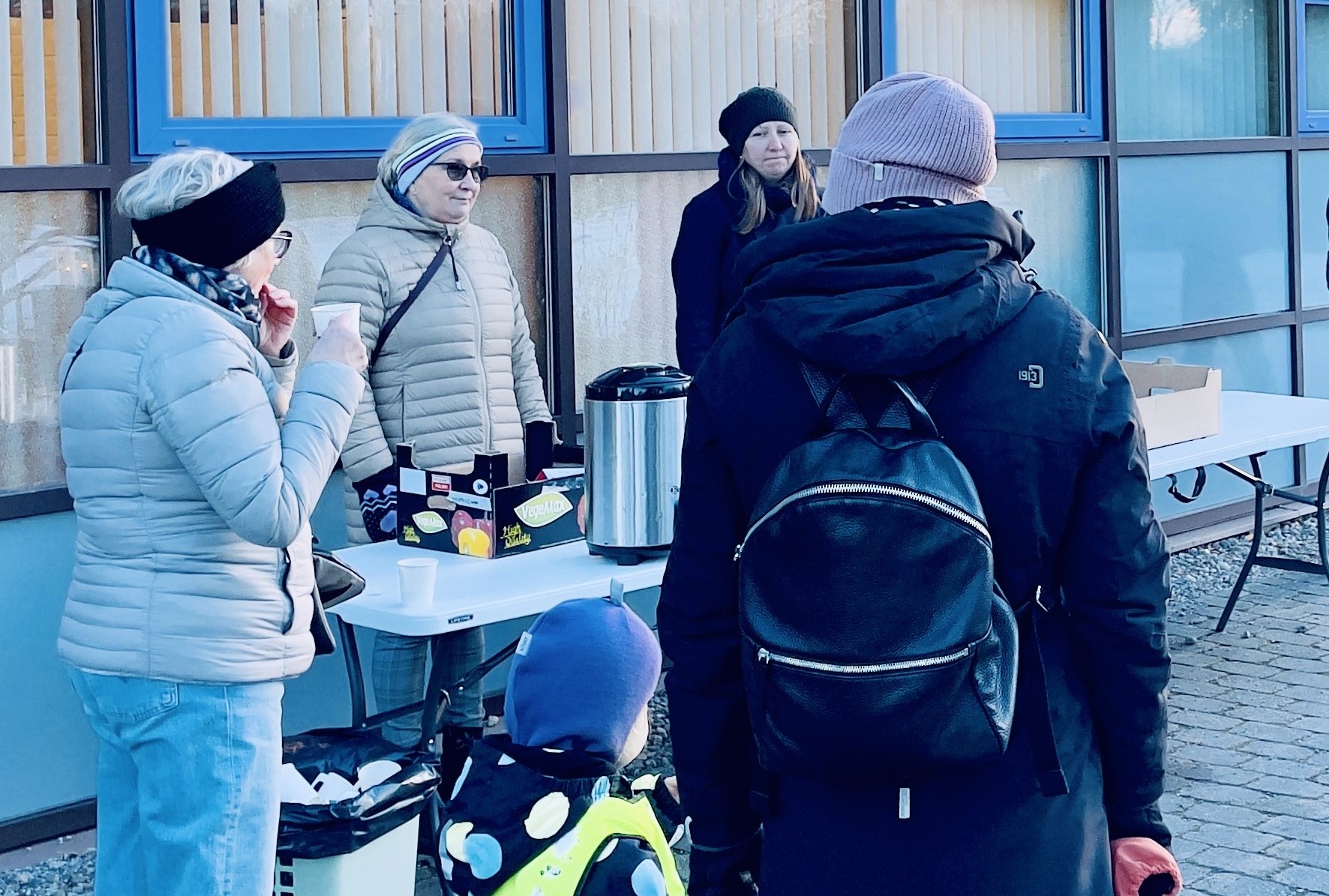 Människro kring ett bord med servering utomhus en kalla dag.