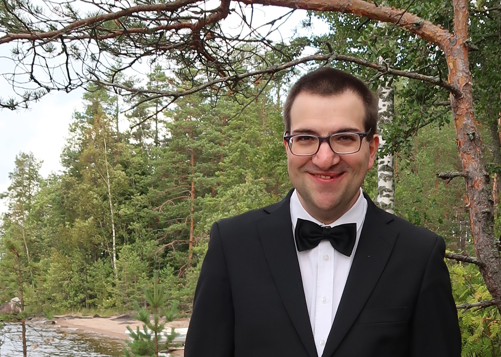 Glad kostymklädd man ute på en skogsbeklädd klippa.