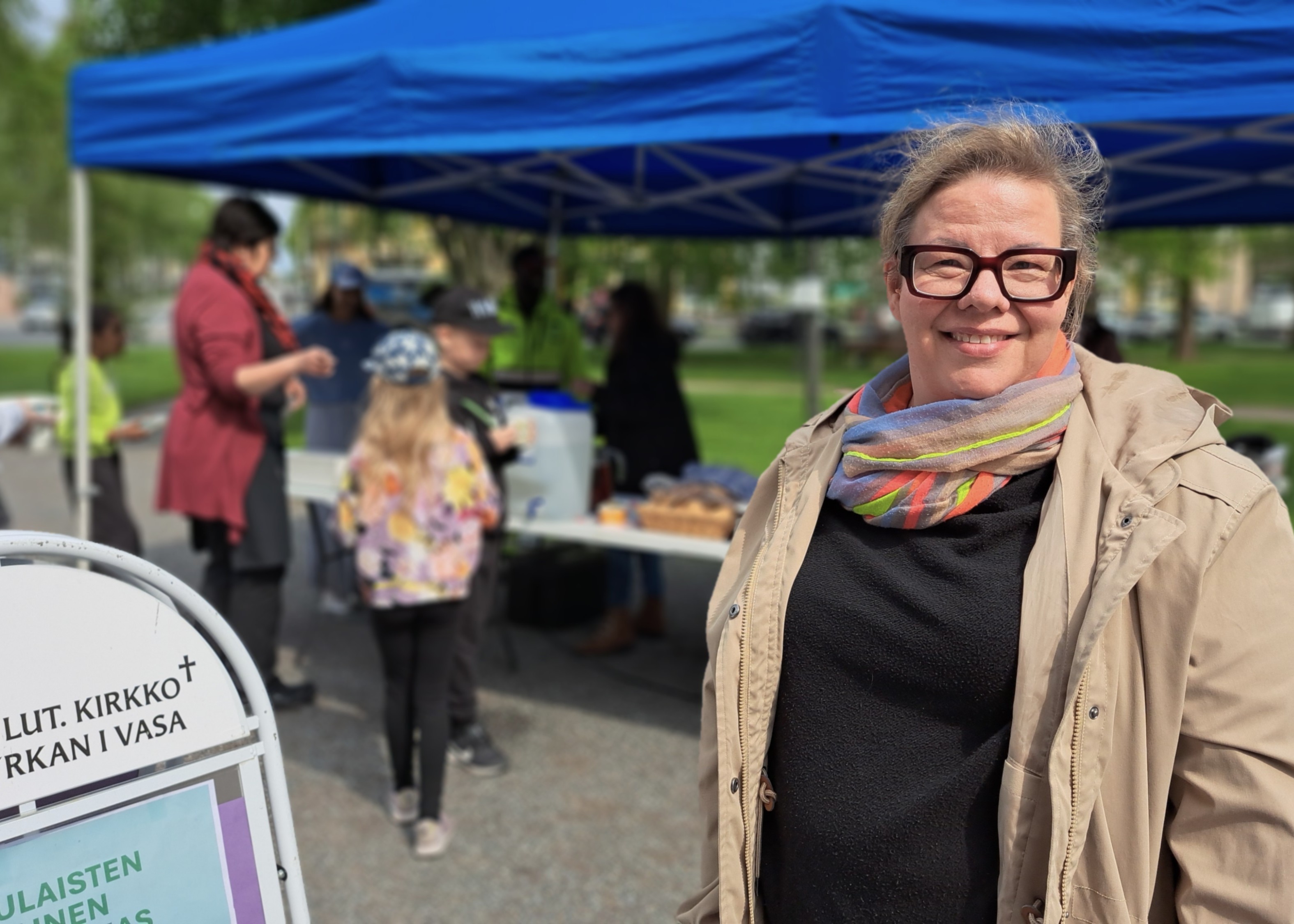 Glad kvinna i en park. I bakgrunden människor.
