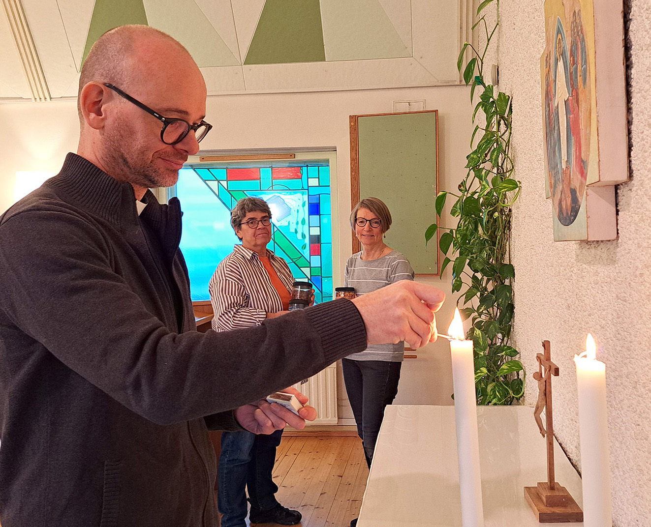 Man tänder ljus på ett altare. I bakgrunden två kvinnor.